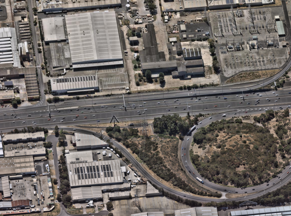 Roadsafe Asphalt’s maintained highway network: aerial view of a multi-lane expressway with steady traffic flow, surrounded by urban development and natural landscapes under clear skies.
